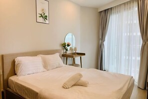 A neatly made bed with a rolled towel, a bedside table with a mirror, and a framed picture on the wall. - 2 Bedroom Luxury Condotel - The Song Vung Tau (Vung Tau)