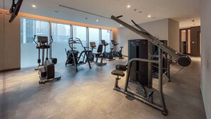 A gym with various exercise equipment, large windows, and a view of the cityscape.