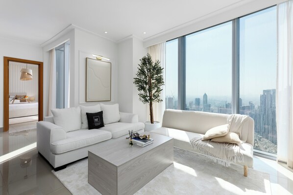 A modern living room with a white sofa, a coffee table, and a large window offering a city view. - Maison Privee - City Heights Retreat w/ Panoramic Skyline Views (Dubai)