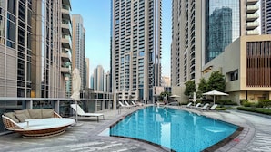 A swimming pool area with lounge chairs and a sofa, surrounded by high-rise buildings.