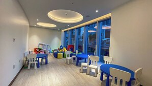 A children's play area with tables and chairs, toys, and a large window with a view of the outside.