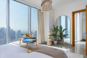 A modern bedroom with a large bed, a bedside table with magazines, a potted plant, and a view of the city through large windows. - Maison Privee - City Heights Retreat w/ Panoramic Skyline Views (Dubai)