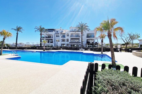 Une piscine à l’eau d’un bleu cristallin, entourée d’une terrasse blanche et de palmiers.