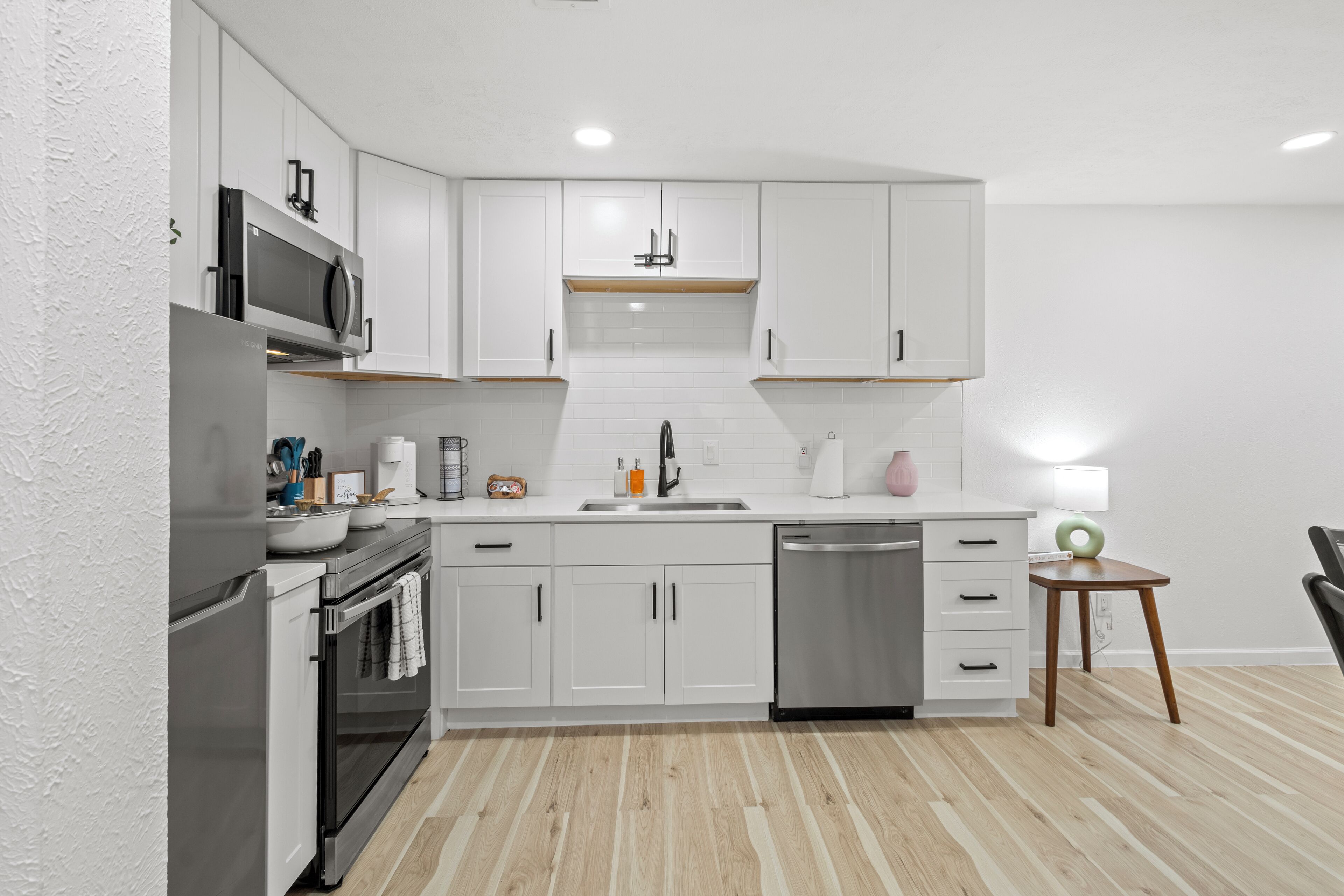A modern kitchen with white cabinets, stainless steel appliances, and a wooden floor.