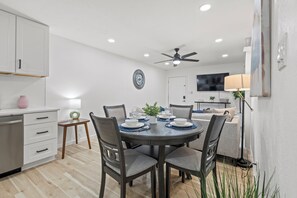 Una cocina moderna con armarios blancos, una mesa de comedor lista para cuatro personas y un ventilador de techo.