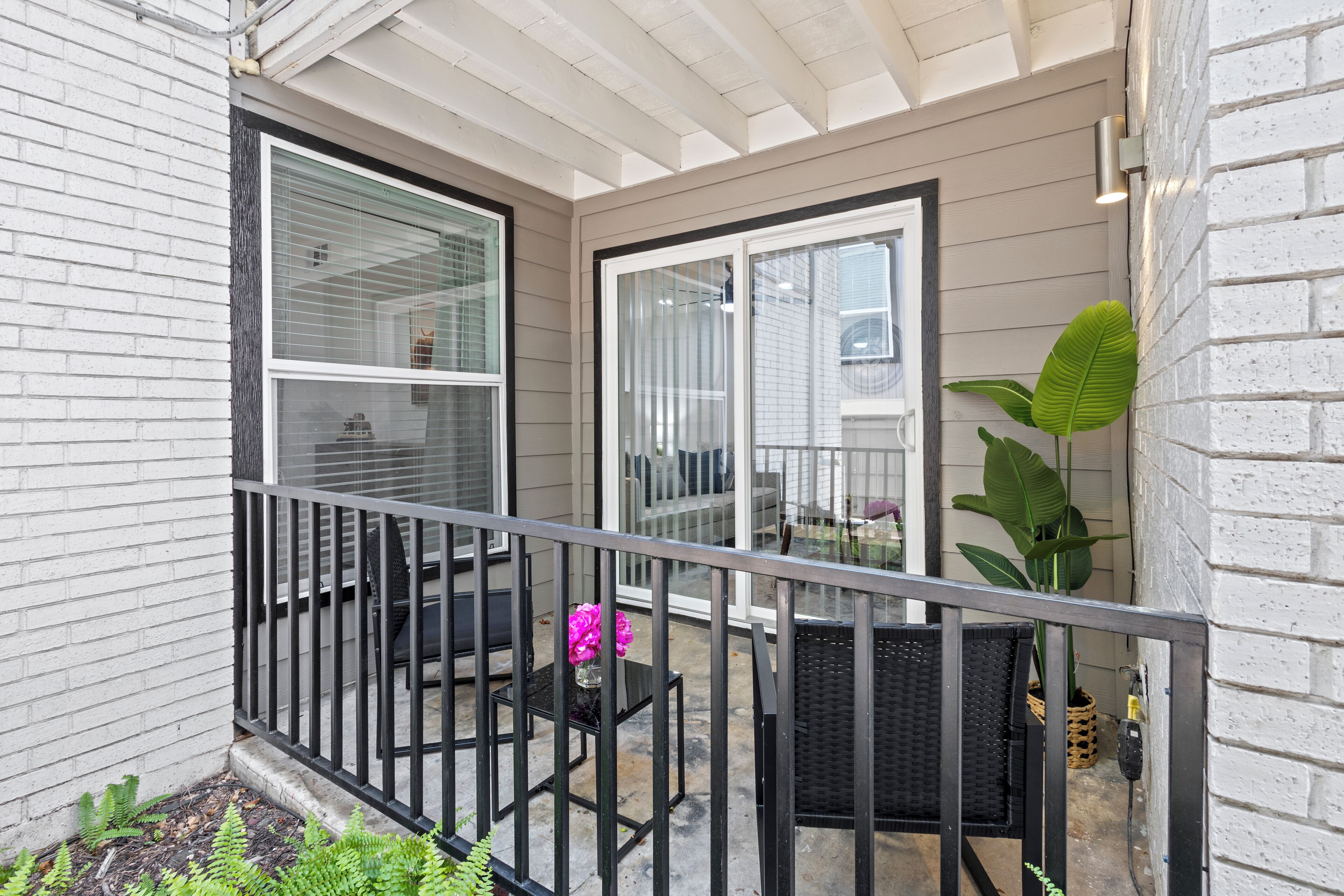 A balcony with a metal railing, a potted plant, and a small table with a vase of flowers.