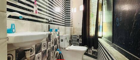 Un bagno con parete rivestita in piastrelle bianche e nere, un lavandino bianco, un water e un secchio rosso.
