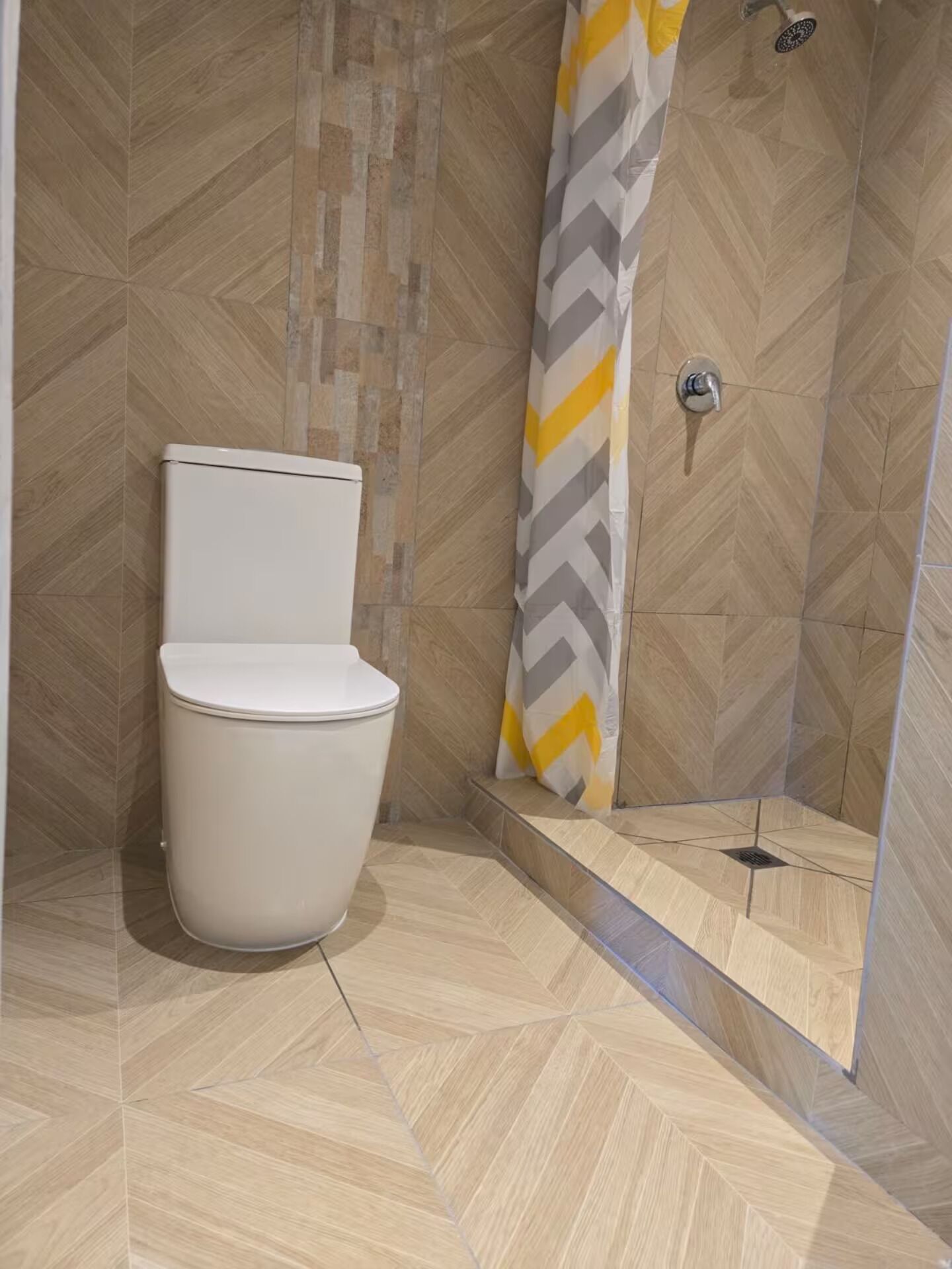Une salle de bain moderne équipée de toilettes, d’une douche et de carreaux disposés en motif de chevron.