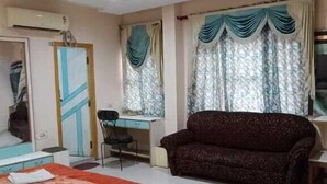 A hotel room with a bed, a desk, a chair, a sofa, and a window with curtains. - Hotel Swaagat (Agra)