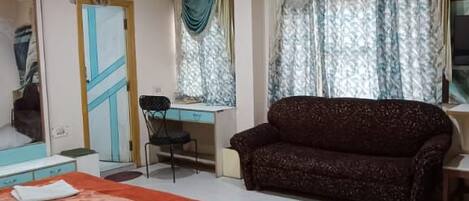 Una habitación de hotel con cama, escritorio, silla, sofá y ventana con cortinas.