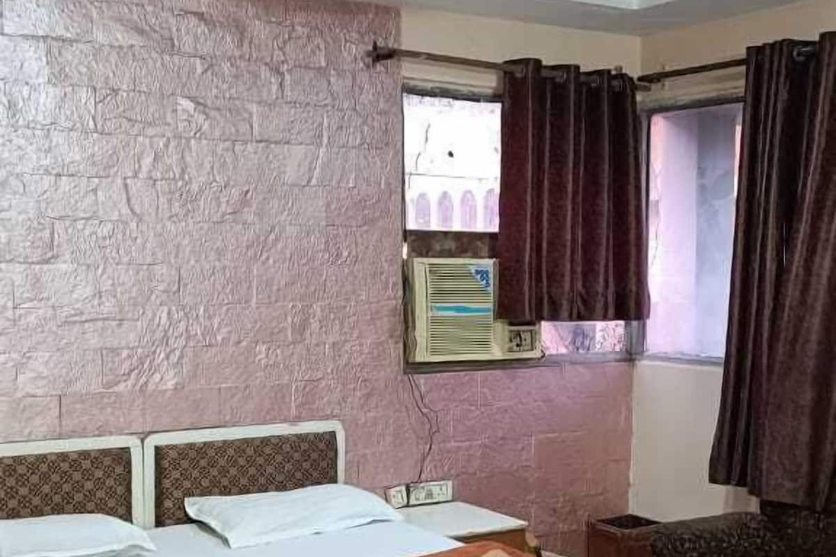 A bedroom with a bed, a window with curtains, a wall-mounted air conditioner, and a ceiling fan.