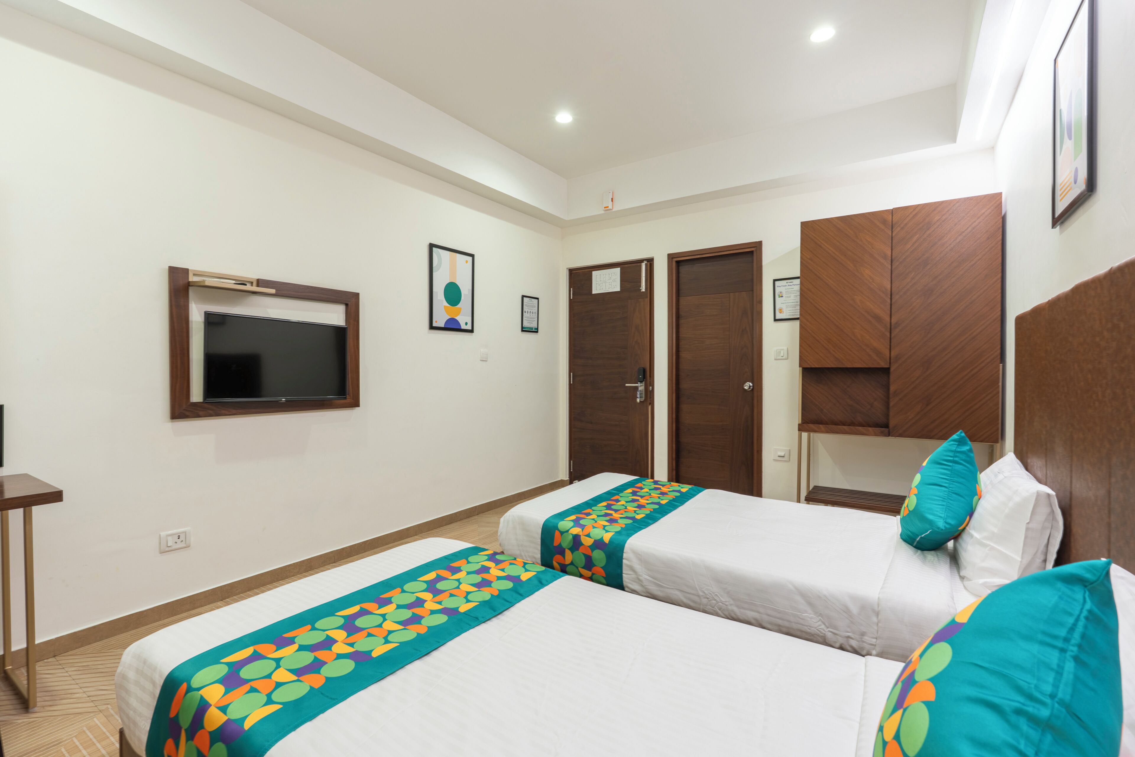 A hotel room with two beds, a TV, wooden wardrobes, and a framed picture on the wall.