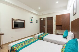 A hotel room with two beds, a TV, wooden wardrobes, and a framed picture on the wall.