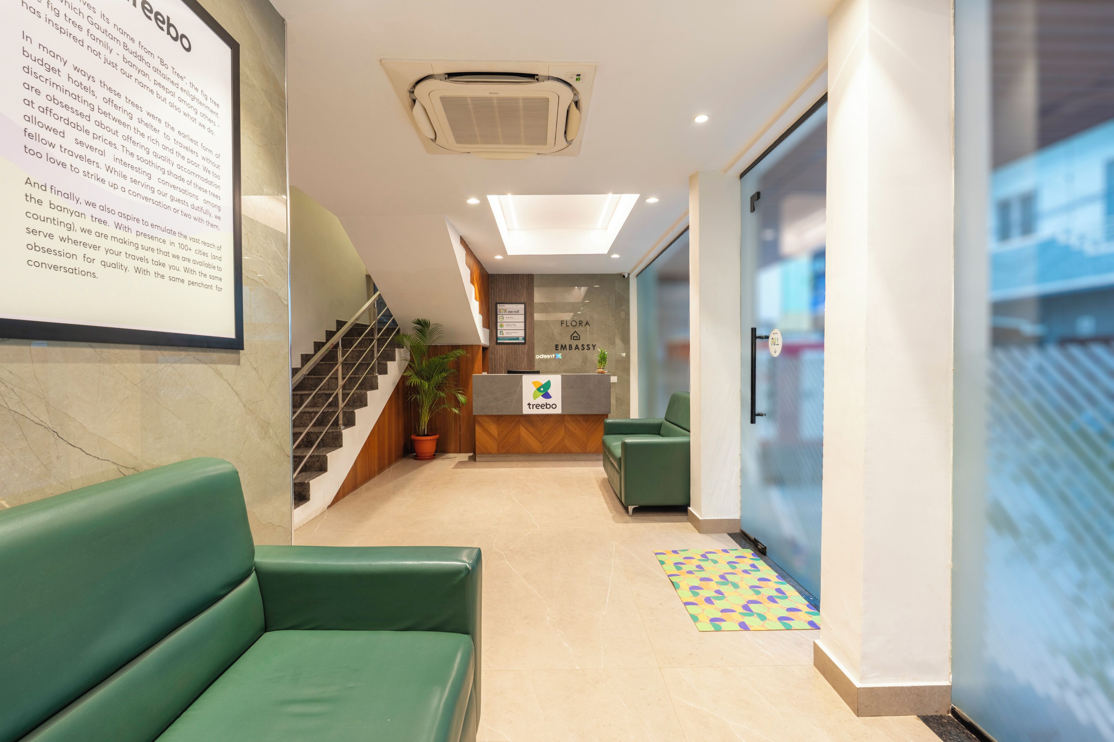 A reception area with a reception desk, green seating, a staircase, and a potted plant.