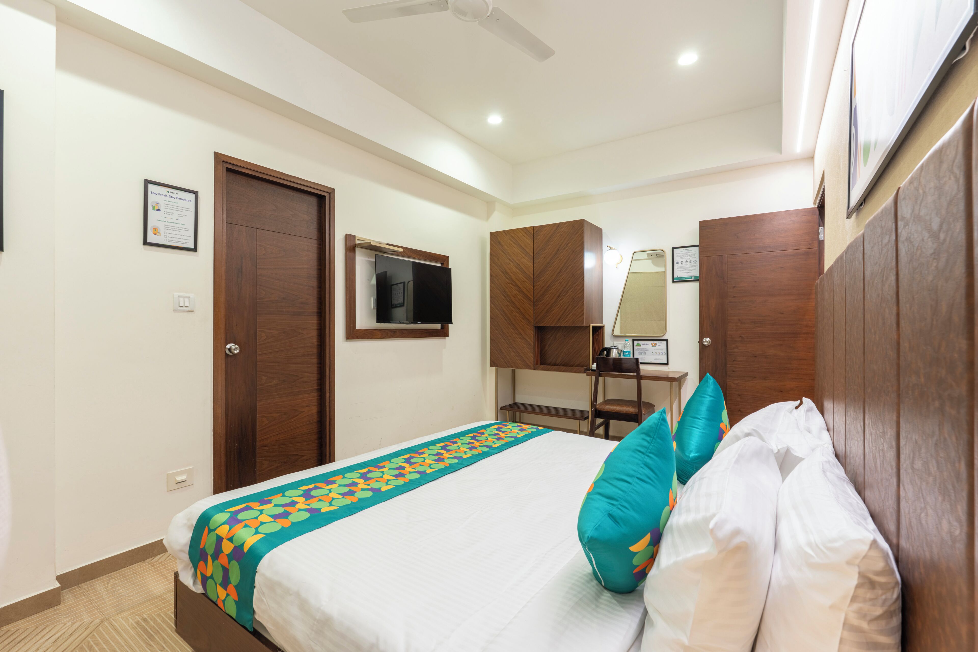 Una camera d'albergo con un letto, una scrivania, una sedia, un armadio e una ventola a soffitto.