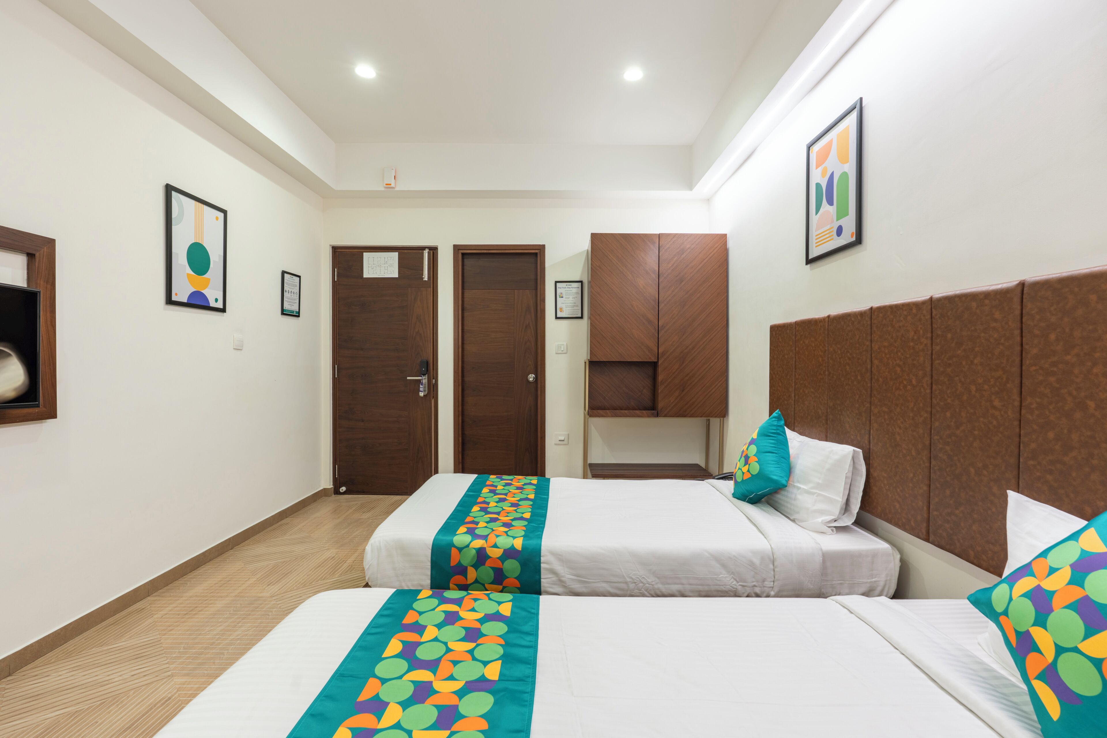 Habitación de hotel con dos camas, cabecera de madera y corredor de cama colorido.