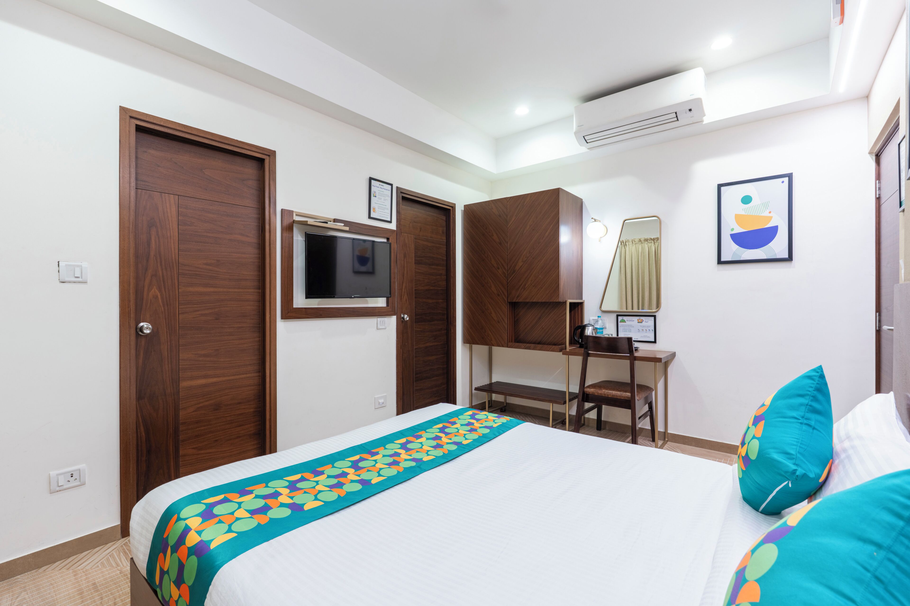 A hotel room with a bed, a desk, a chair, a TV, and a wardrobe.