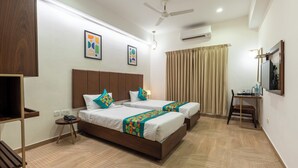 A hotel room with two beds, a desk, a chair, a ceiling fan, and an air conditioning unit. - Treebo Flora Embassy (Chennai)