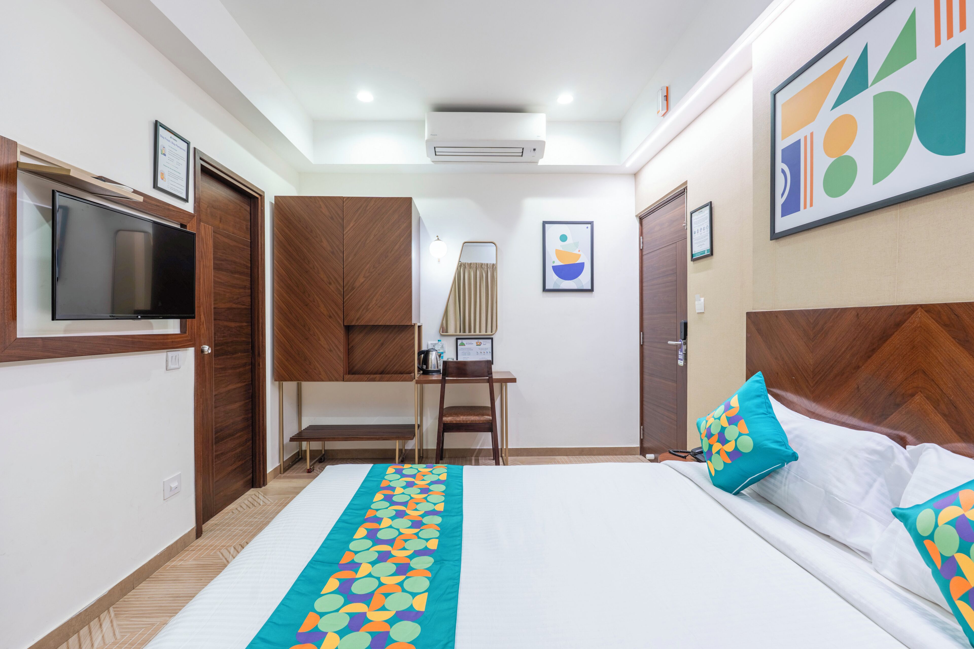 Habitación de hotel con cama, escritorio, silla, televisor y un cuadro en la pared.