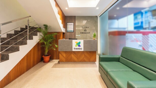 A reception area with a reception desk, a staircase, a green sofa, and a potted plant. - Treebo Flora Embassy (Chennai)