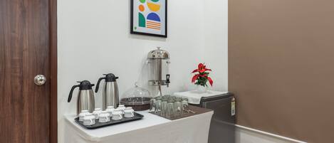 A breakfast bar with coffee makers, cups, and a refrigerator.