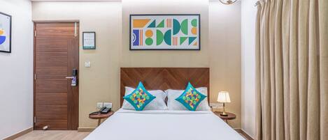 A hotel room with a bed, a wooden headboard, a framed abstract artwork, a bedside table with a lamp, and a door.