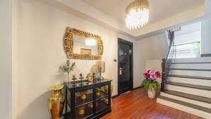 A hallway with a wooden floor, a black console table with decorative items, a mirror with a gold frame, and a staircase with a railing. - Rachamankha Flora House Chiang Mai (Chiang Mai)