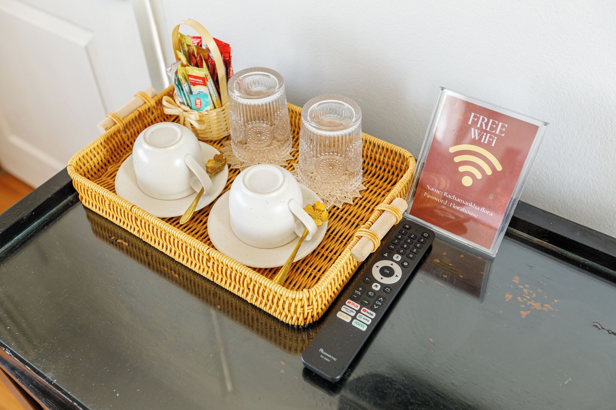 A tray with teacups, glasses, and a remote control on a glass table.