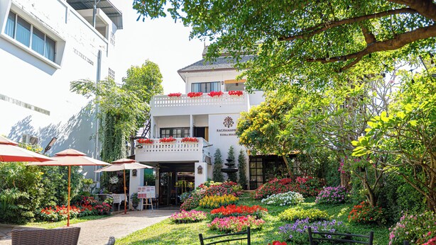 A garden with a variety of flowers and plants, outdoor seating with umbrellas, and a building with a sign that reads "RACHAMANKIN FLORA HOUSE". - Rachamankha Flora House Chiang Mai (Chiang Mai)