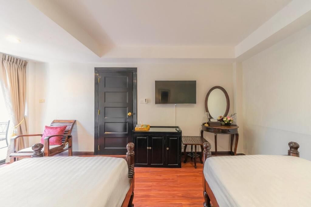 A hotel room with two beds, a wooden wardrobe, a desk with a mirror, and a television on the wall.