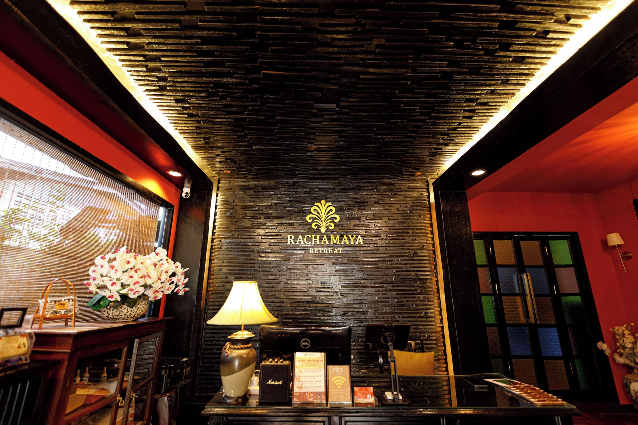 A reception area with a dark textured wall, a reception desk, a lamp, and a floral arrangement.