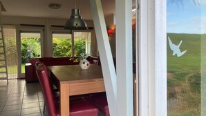 A dining area with a wooden table, red chairs, a vase with flowers, and a view of greenery through a window. - 6 pers - Modern holiday home with garden, close the Lauwersmeer (Eanjum)