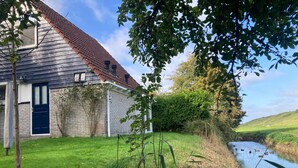 A house with a blue door, a brick exterior, and a grassy yard adjacent to a water body. - 6 pers - Modern holiday home with garden, close the Lauwersmeer (Eanjum)