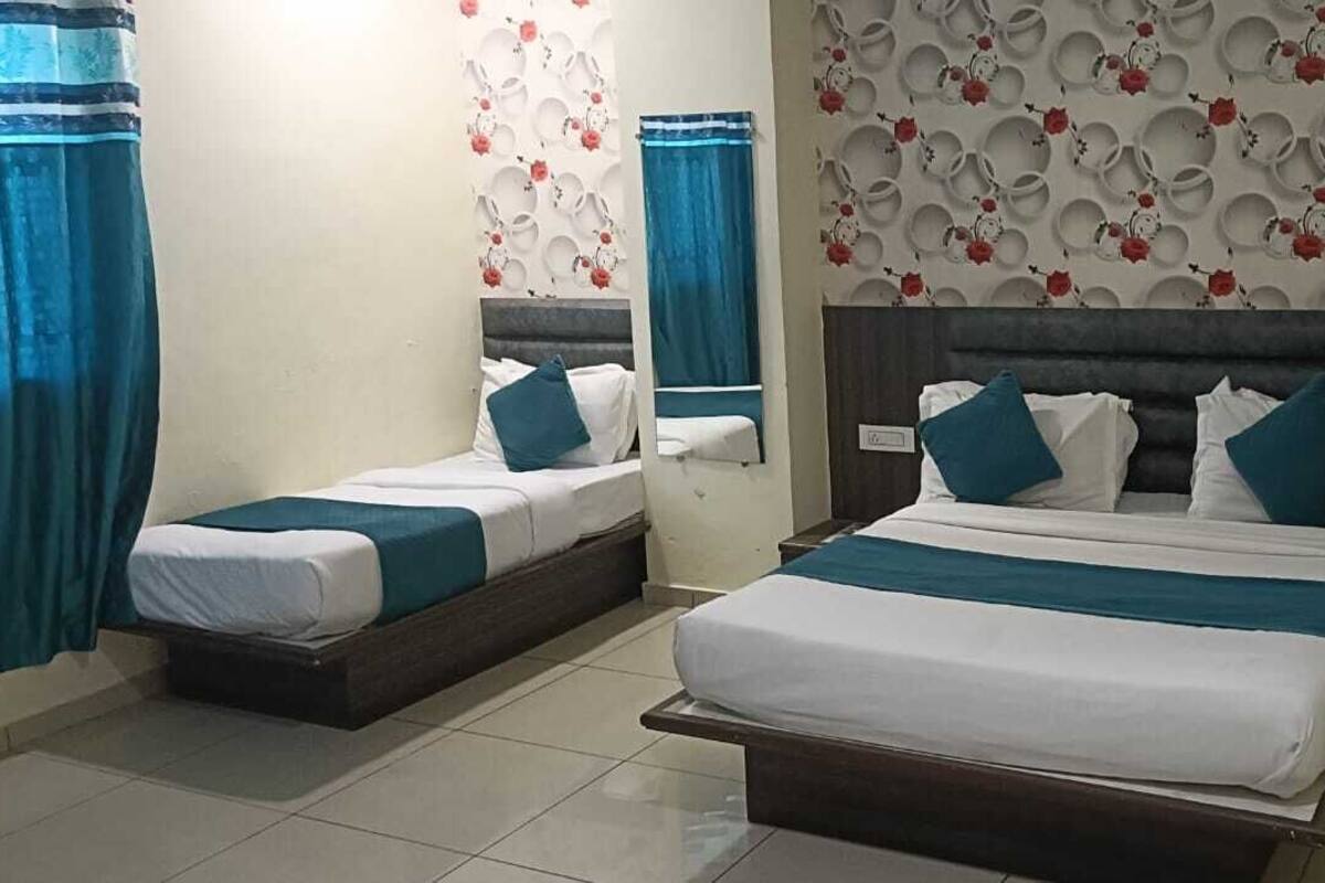 Habitación de hotel con dos camas, cada una con ropa y almohadas color turquesa, un espejo grande y un papel tapiz con estampado floral.