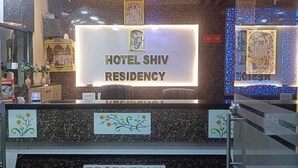 Una recepción en el Hotel Shiv Residency con un letrero encima, una barra con diseño decorativo y una pared con obras de arte enmarcadas.