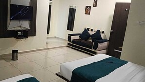 Una habitación de hotel con cama, sofá, televisión montada en la pared y un cubo de basura.