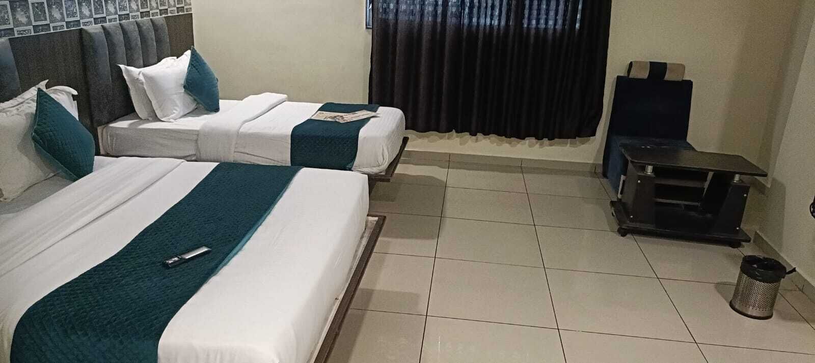 A hotel room with two beds, a small table, a chair, and a trash bin.