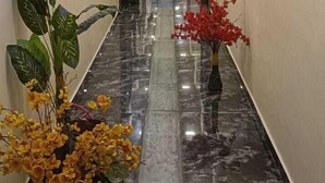 Un largo pasillo estrecho con suelo de mármol pulido, flanqueado por paredes blancas e iluminado por luces del techo.