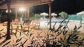 Ett utomhusområde som är öppet på kvällen och natten, med en pool, solstolar och en överbyggd sittplats med bord och stolar.