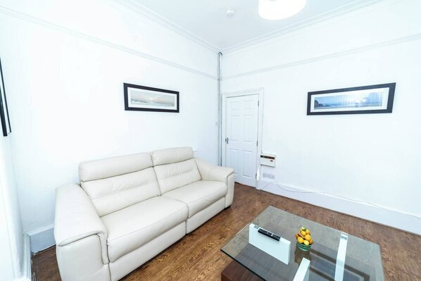 A living room with a beige sofa, a glass coffee table, and two framed pictures on the walls.