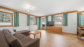 A spacious living room with a sofa set, a wooden coffee table, a television, and a dining area with a bench and chair. - Apartment in a quiet location in Mittersill (Mittersill)