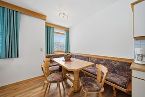 A dining area with a wooden table and chairs, a bench with floral upholstery, and a view through a window with curtains.