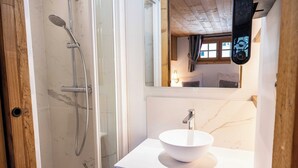 Un baño con ducha compartimentada con vidrio, lavamanos de mármol blanco y tocador de madera.