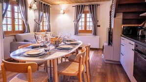 Un comedor con una mesa redonda preparada para cuatro, sillas de madera, un sofá y una zona de cocina con electrodomésticos modernos.