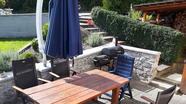 An outdoor patio with a wooden table and chairs, a grill, and a blue umbrella. - Apartment 'Sammet' with Shared Terrace, Communal Garden and Wi-Fi (Brilon)