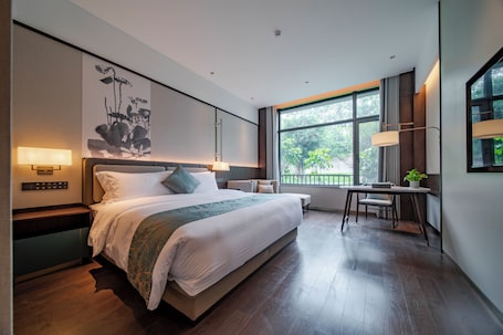 A modern hotel room with a large bed, bedside lamps, a desk, and a view of greenery outside.. Yingbin Hotel