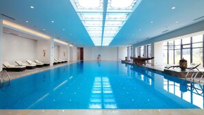 Una piscina interior con agua azul cristalina, techo de tragaluces y ventanas iluminadas por el sol.