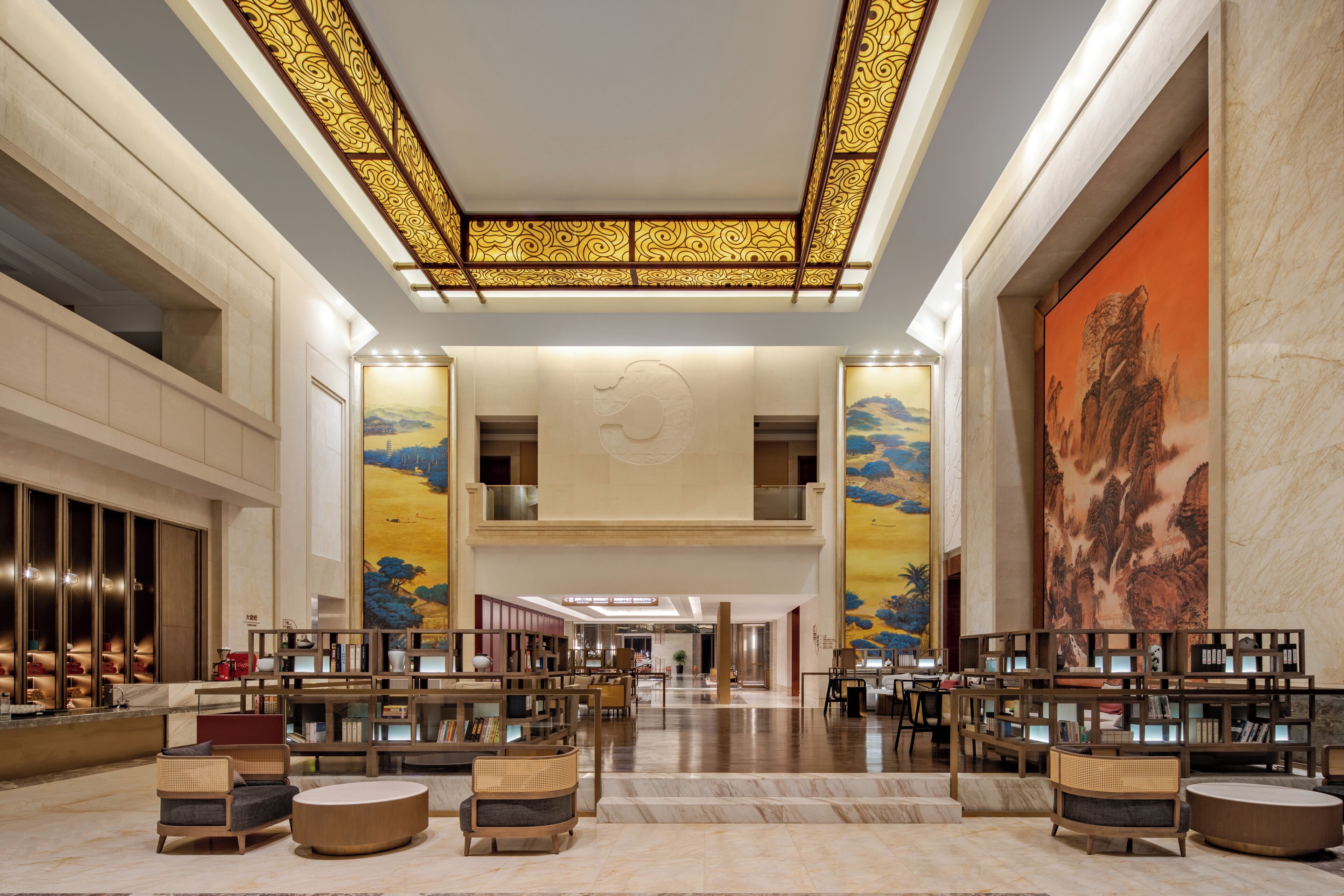 Um lobby amplo com teto alto, escadaria central e um grande mural na parede direita.