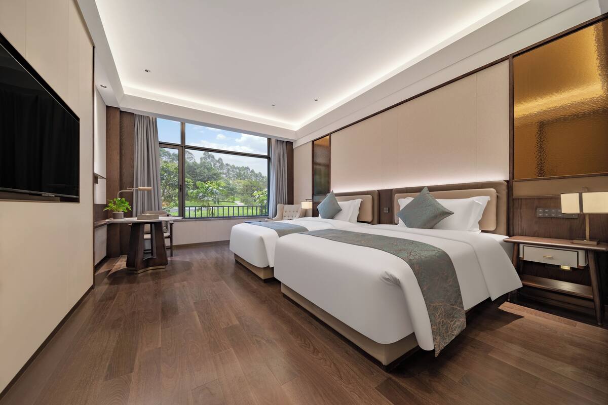 A modern hotel room with a large bed, a desk, a chair, and a TV.