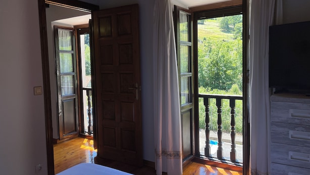 A room with a bed, a wooden door, and a balcony with a view of greenery. - La Casina del Arroyo, rural cottage for 2-4 people in Poo de Cabrales (Póo de Cabrales)